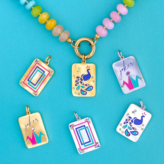 A set of colorful rectangular enamel charms with peacock and crown designs, displayed on a bright turquoise background. One charm is attached to a beaded necklace with pastel beads and a gold clasp, while five other charms are shown individually below it.