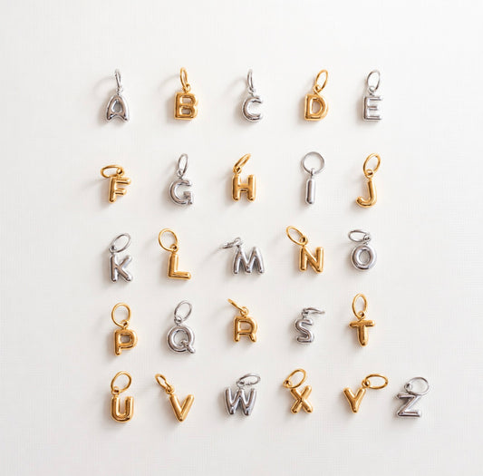 Twenty-five small alphabet letter charms arranged in a grid on a plain white background. Each charm is made of two-tone metal, alternating between polished gold and silver finishes.
