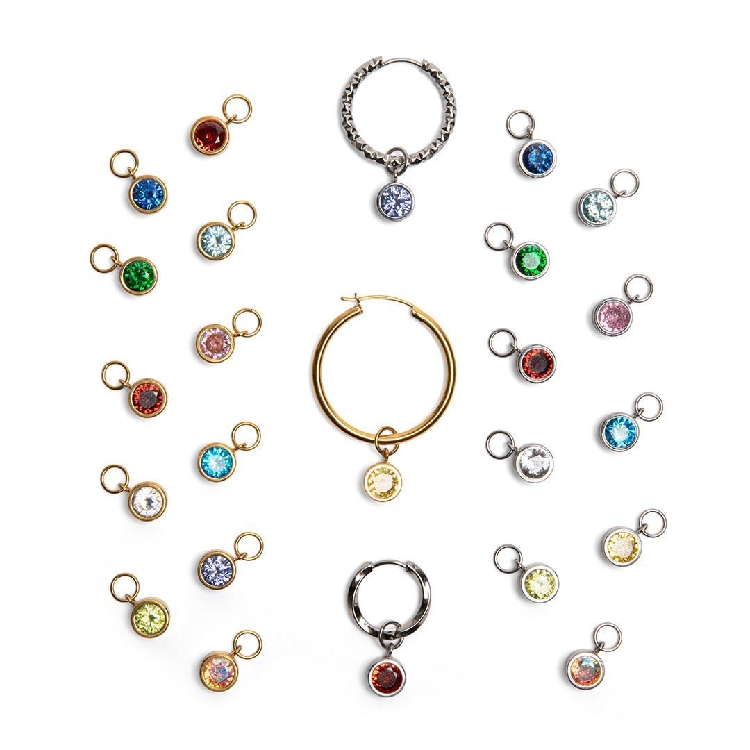 A set of small round gemstone charms in gold, silver, and rose gold tones, arranged around two larger hoop-style pieces on a plain white background.