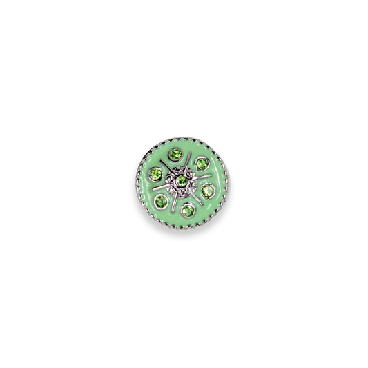 A round silver-toned dot featuring a light green enamel center, surrounded by small green gemstones and a silver floral starburst design, set against a plain white background.