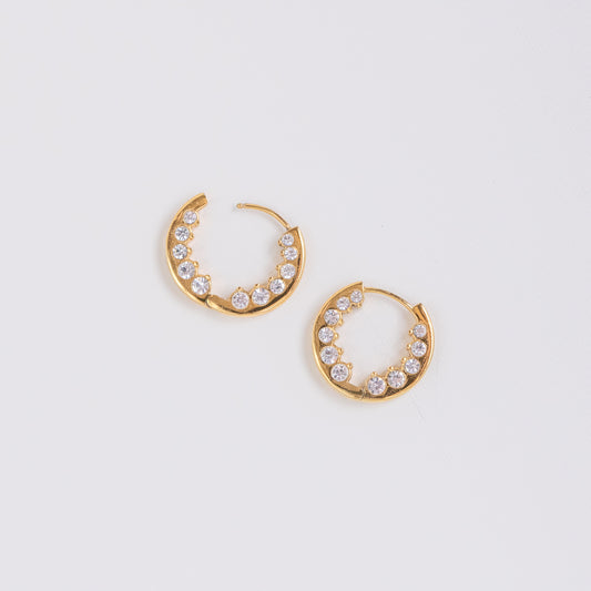 A pair of gold crescent-shaped hoop earrings adorned with small clear round stones, displayed on a clean white background.