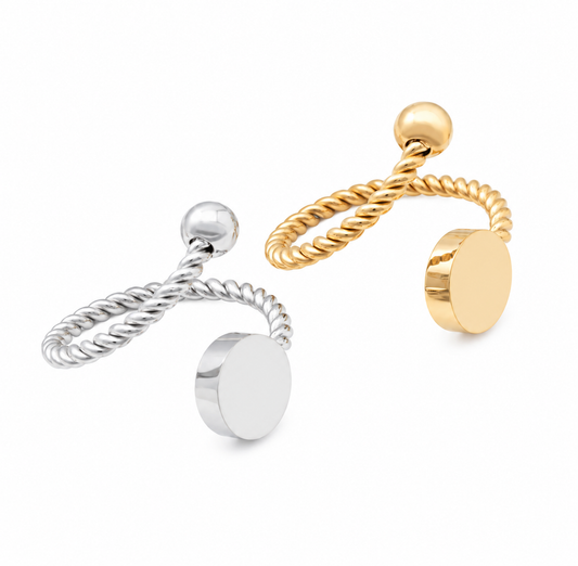 Two minimalist rings on a white background, one in polished silver and one in polished yellow gold color. Each features a twisted rope band, a small spherical bead, and a flat circular disc that can be engraved.
