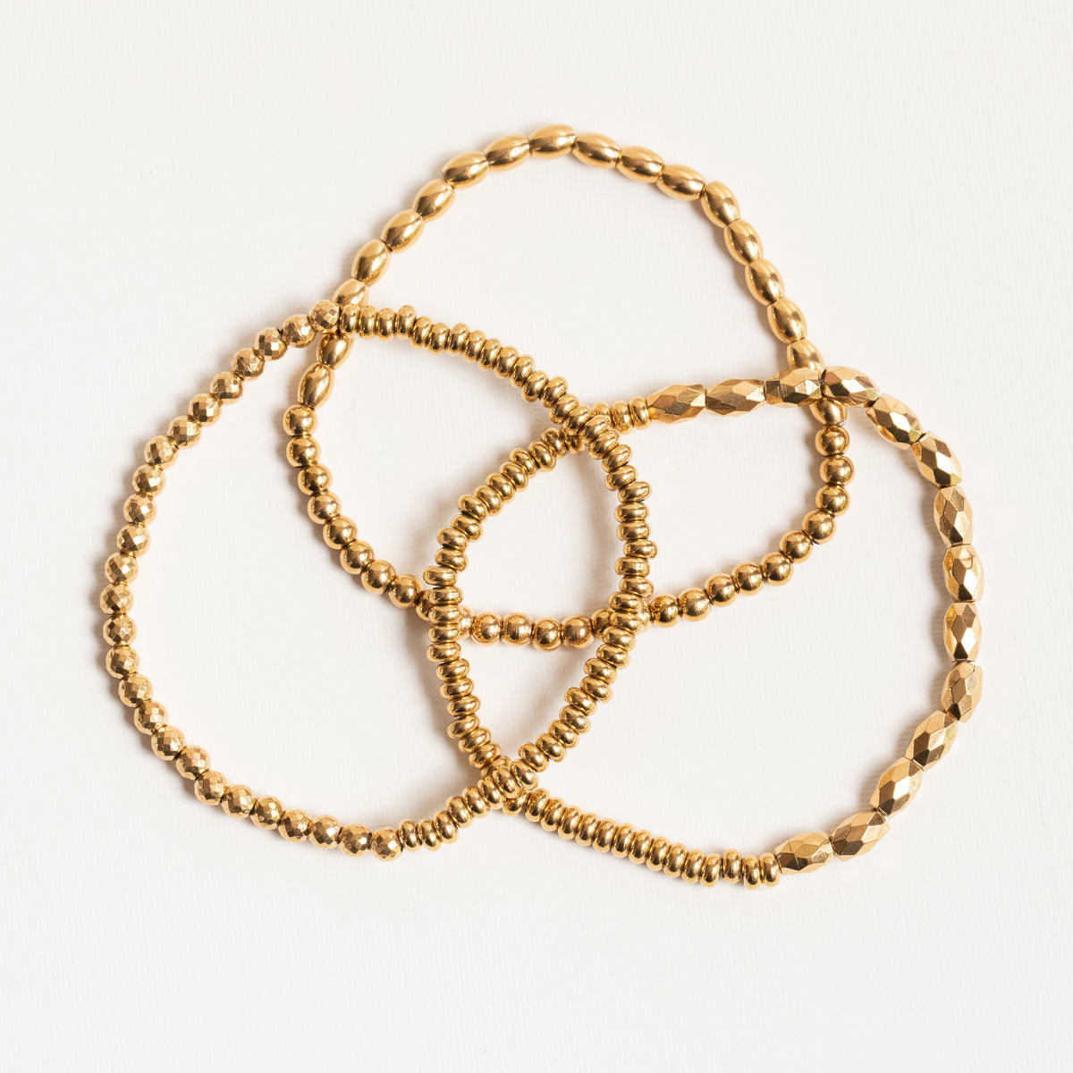 Three gold-toned beaded and faceted chain bracelets arranged in a loose circle on a clean white background.