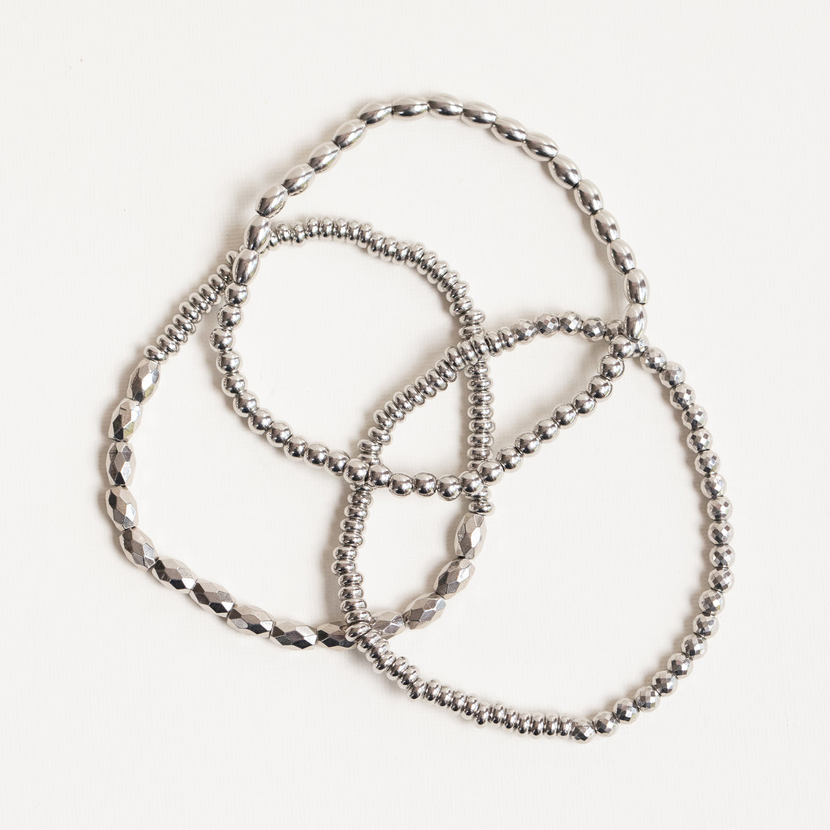 A set of three silver-toned beaded bracelets with different link patterns, arranged on a plain white background.