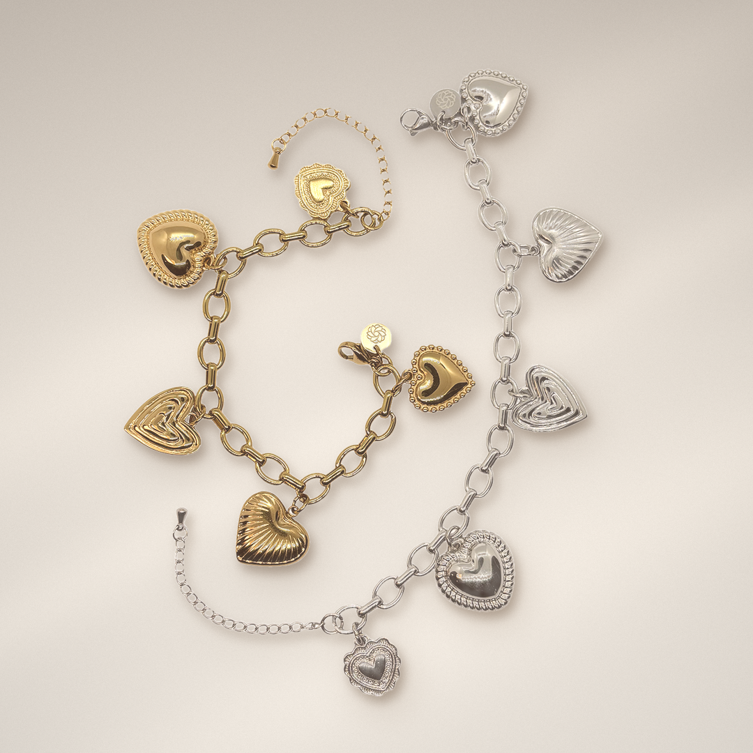 Two heart-themed charm bracelets displayed on a light beige background. One bracelet is gold with textured and polished heart charms, and the other is silver with matching heart charms. 