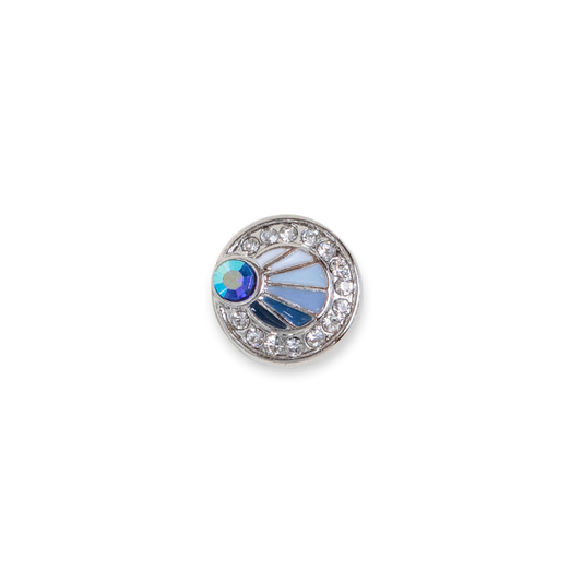 A round silver-toned Dot featuring a halo of clear crystals and a central sunburst design with light blue enamel, a blue iridescent crystal, set against a plain white background. This size is the Dotlet size released in September/ October 2026