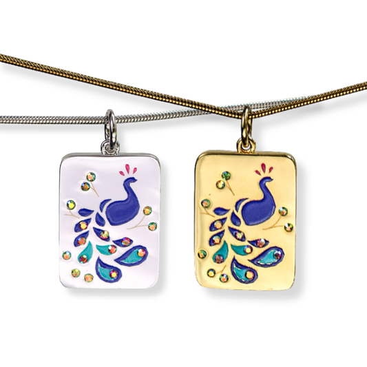 Two rectangular pendant necklaces with peacock designs hang from chains against a white background. One pendant has a white background with a blue peacock and multicolored tail details, and the other has a gold background with a matching peacock design.