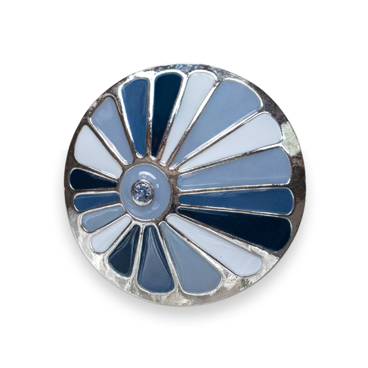A round Statement Dot featuring a sunburst design with alternating light blue, navy blue, and white enamel segments, set in a silver-tone metal with a small clear stone at the center, shown on a white background.