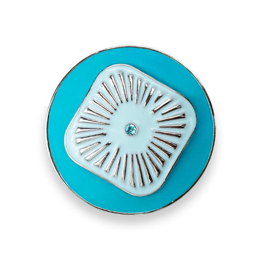A round turquoise blue enamel Dot with a central light blue square design featuring radiating silver metal lines and a small blue crystal in the center, shown on a white background.