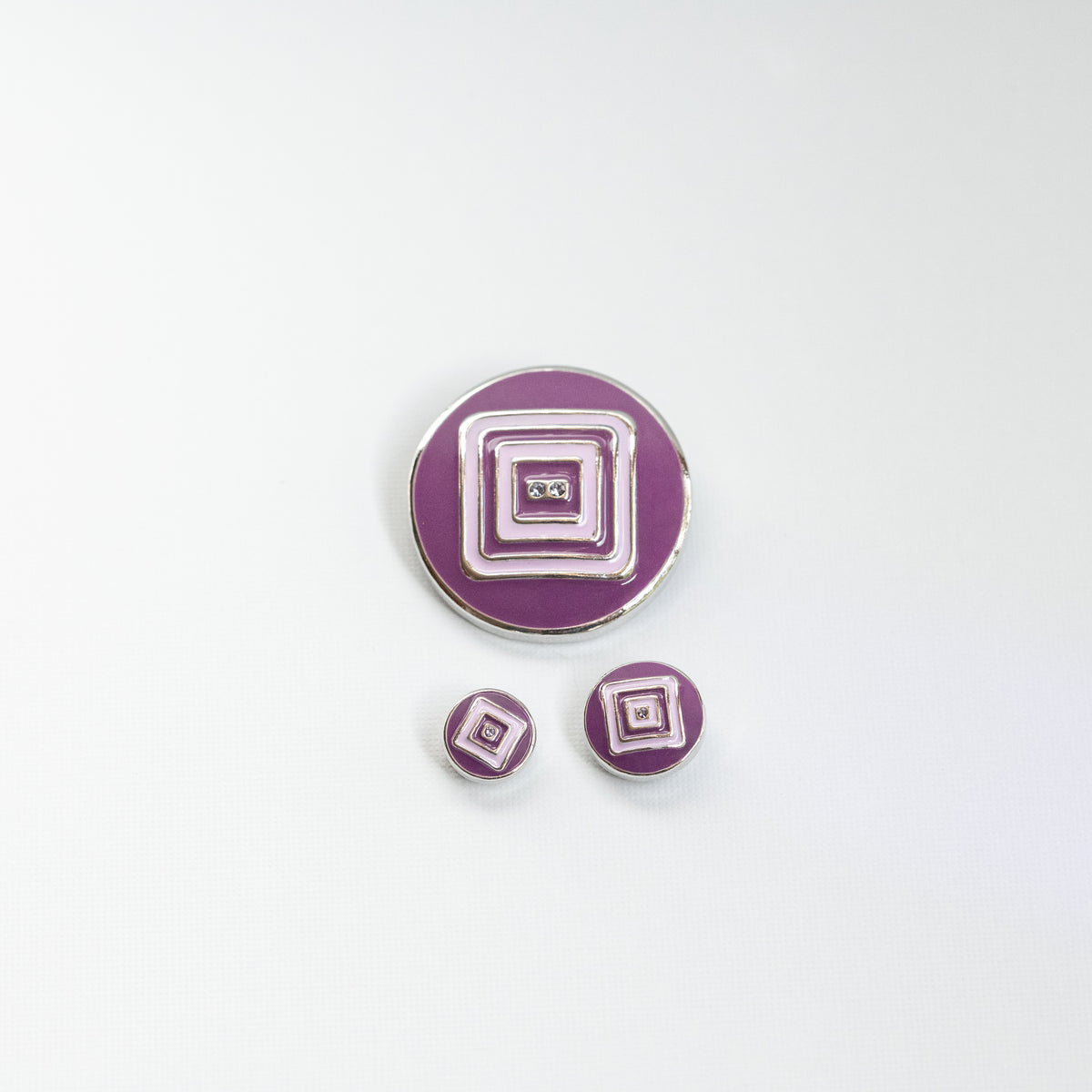 A set of 3 round purple enamel Dots,  with concentric square and rectangular geometric patterns in the middle, outlined in silver-tone metal, featuring two small clear rhinestones at the center, shown on a white background.